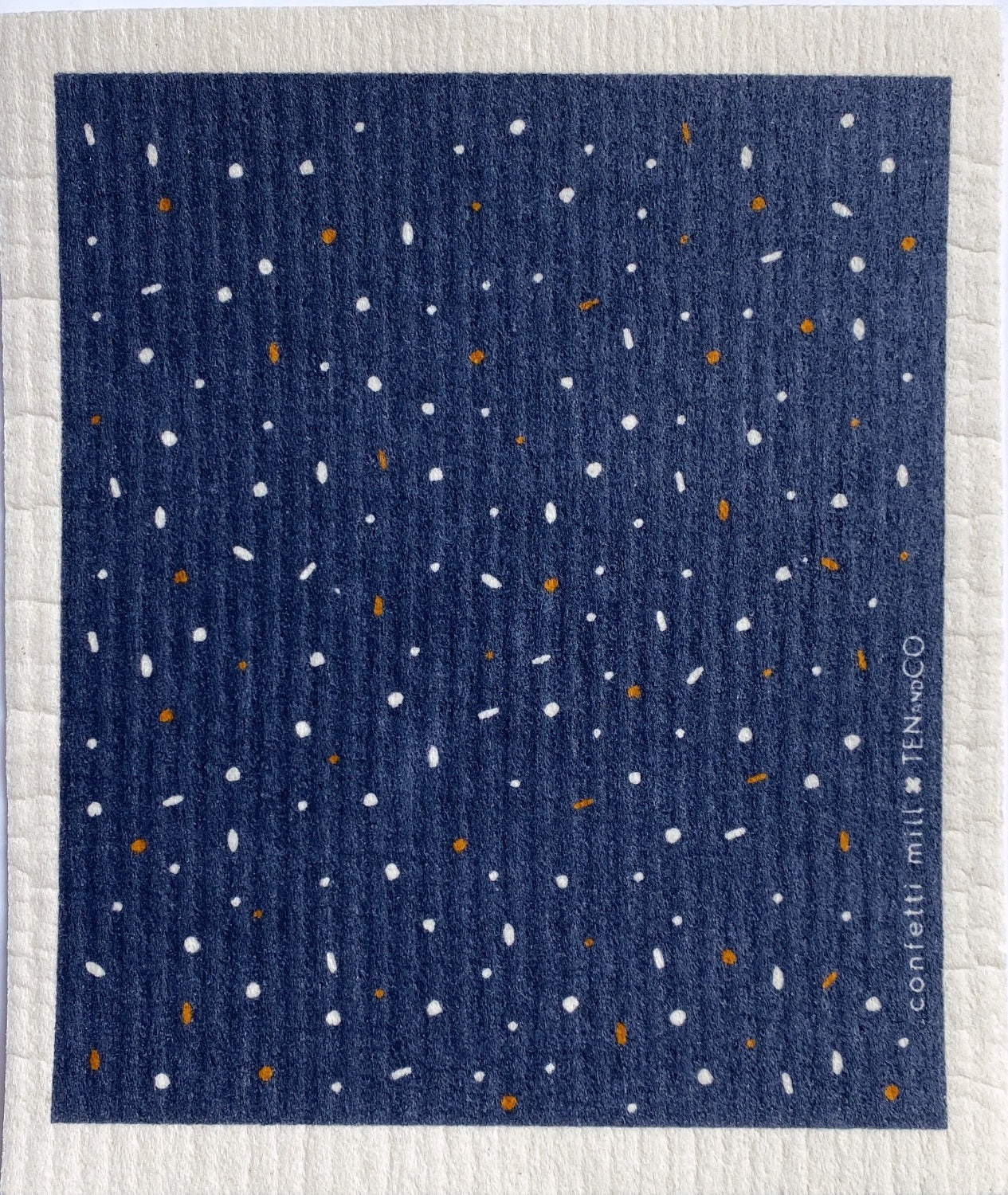 Birds eye view image of 1 of 2 Confetti Mill sponge cloths. The sponge cloth has a dark blue background with white and mustard yellow confetti and a white border.