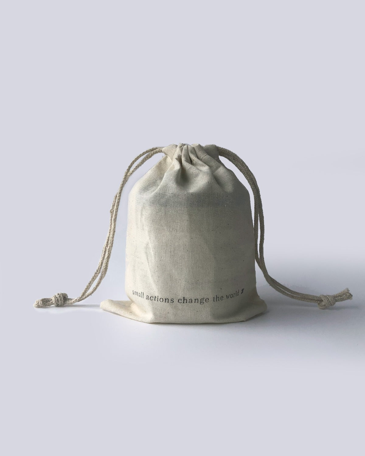 Product image of Reusable Cotton Drawstring Bag. This image is of the back of the bag. The bag is a beige cotton with the words “small actions change the world” in black font at the bottom. There are strings coming out of either side of the top and the bag is closed tight. 