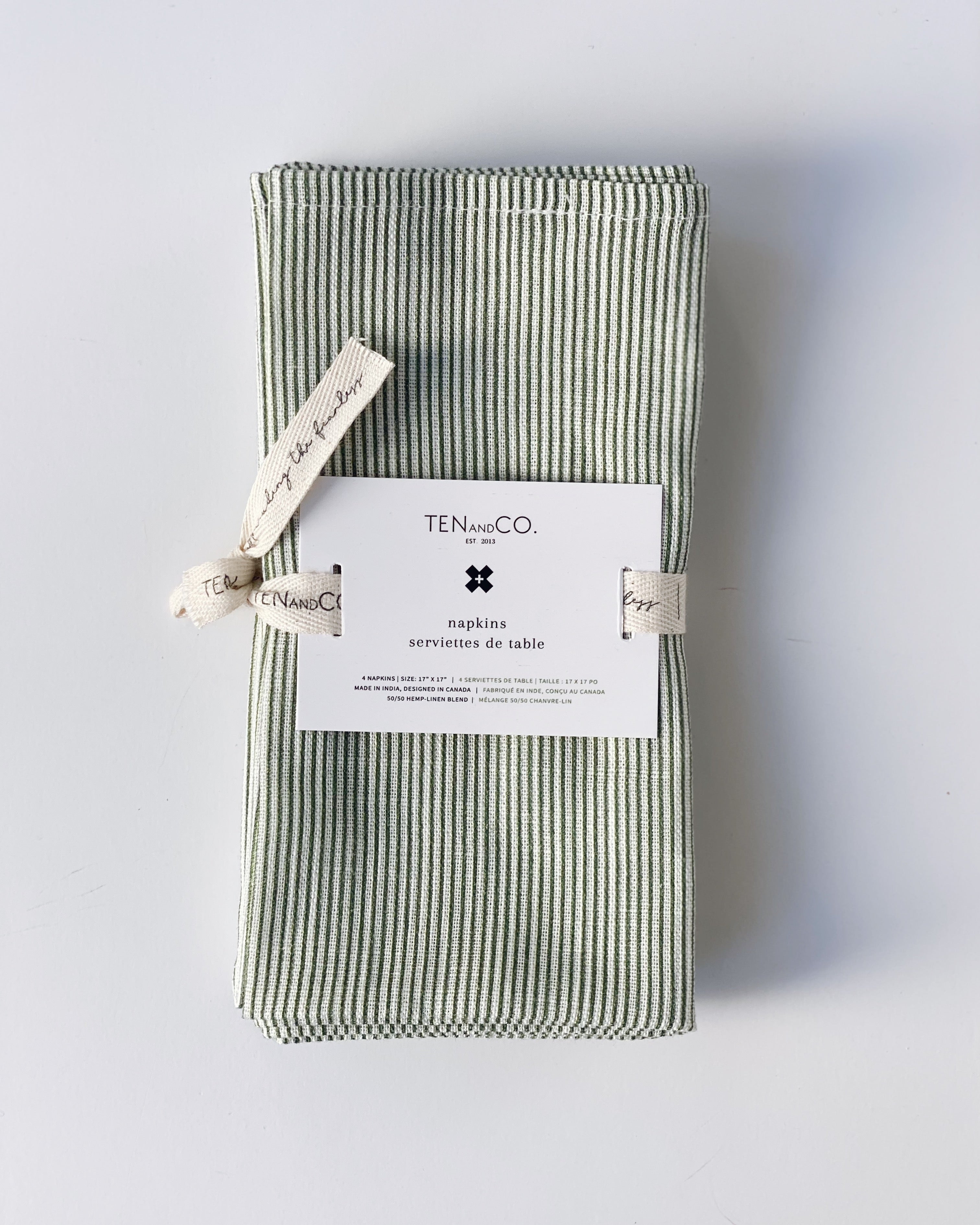 Flat lay image of Stripes Sage, 4 set of Napkins on a white background. The napkins have a white base colour with stripes of green covering the entirety of the cloth and are tied together with Ten and Co twill tape and a recyclable paper tag laying on top.