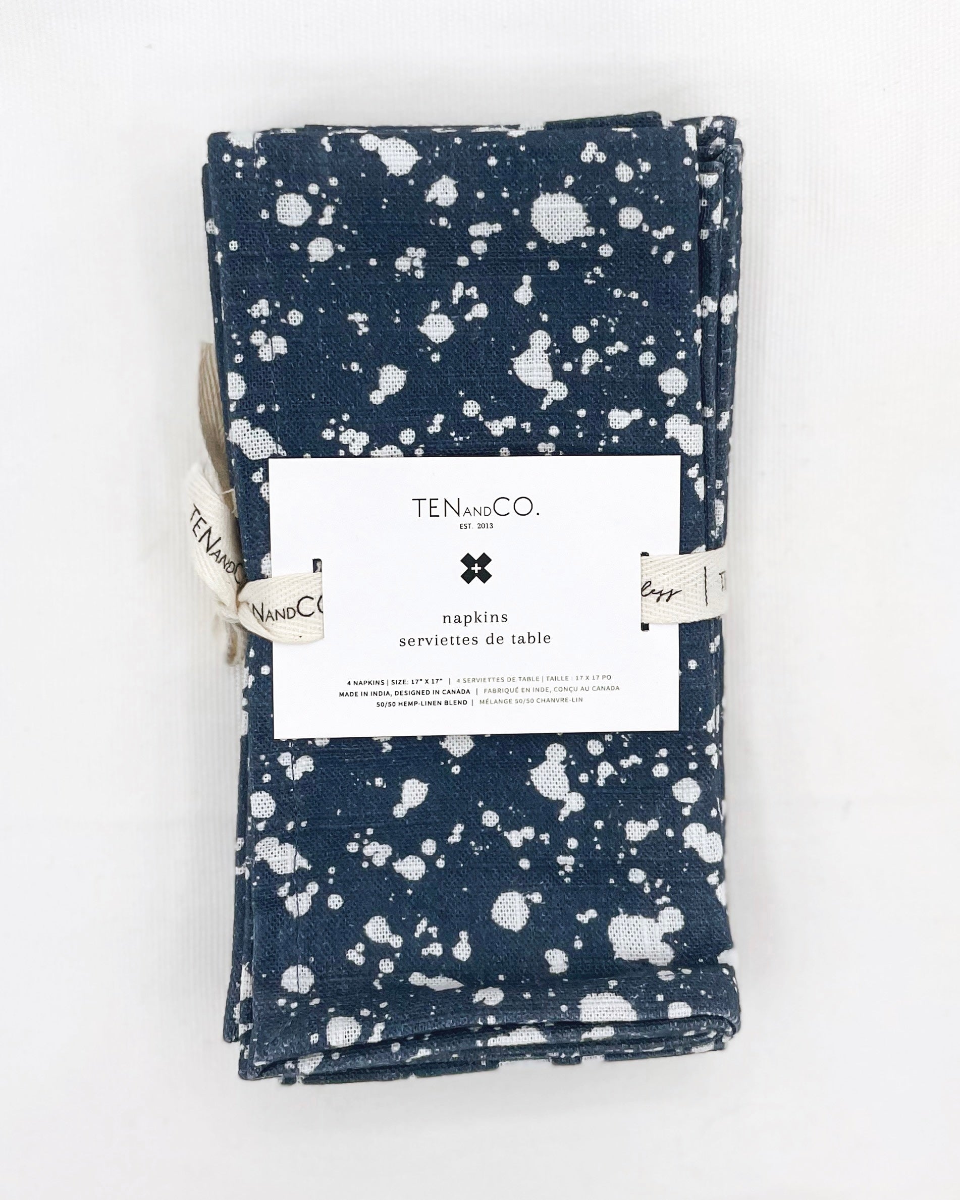 Flat lay image of Splatter Denim, 4 set of Napkins on a white background. The napkins have a deep blue base colour with splatters of white covering the entirety of the cloth and are tied together with Ten and Co twill tape and a recyclable paper tag laying on top.