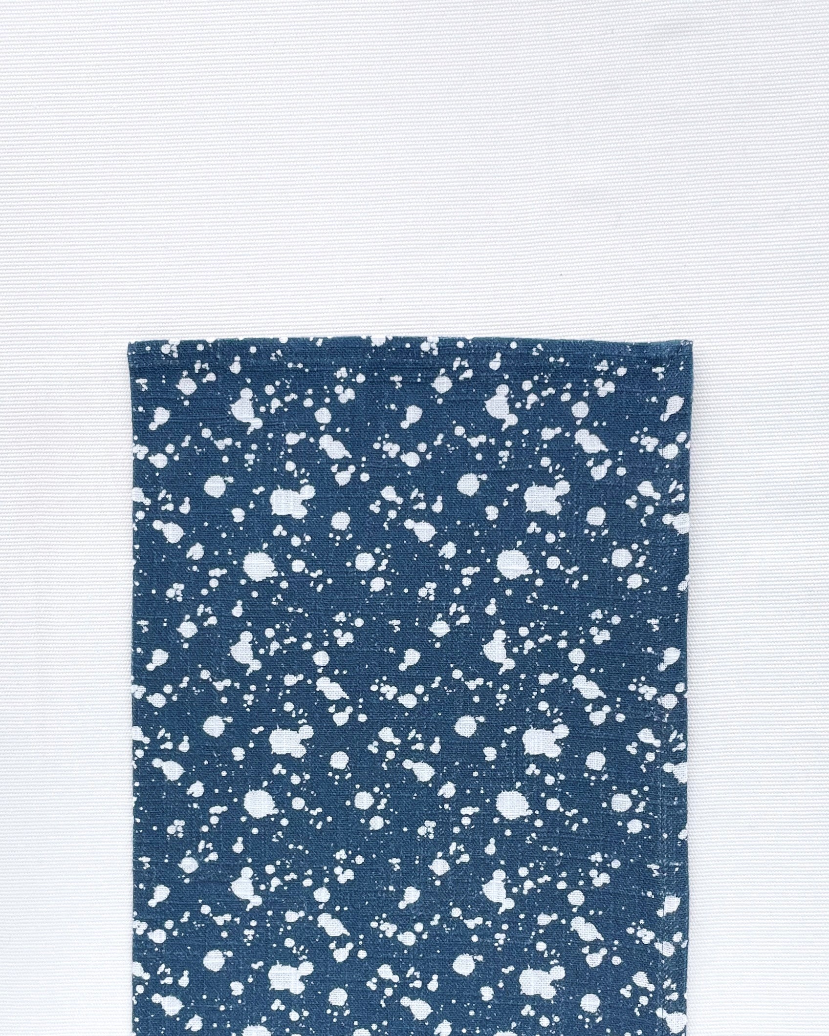 Flat lay of Splatter Denim Napkin folded in half on a white background.  Napkin is navy blue with white spots splattered all over it.