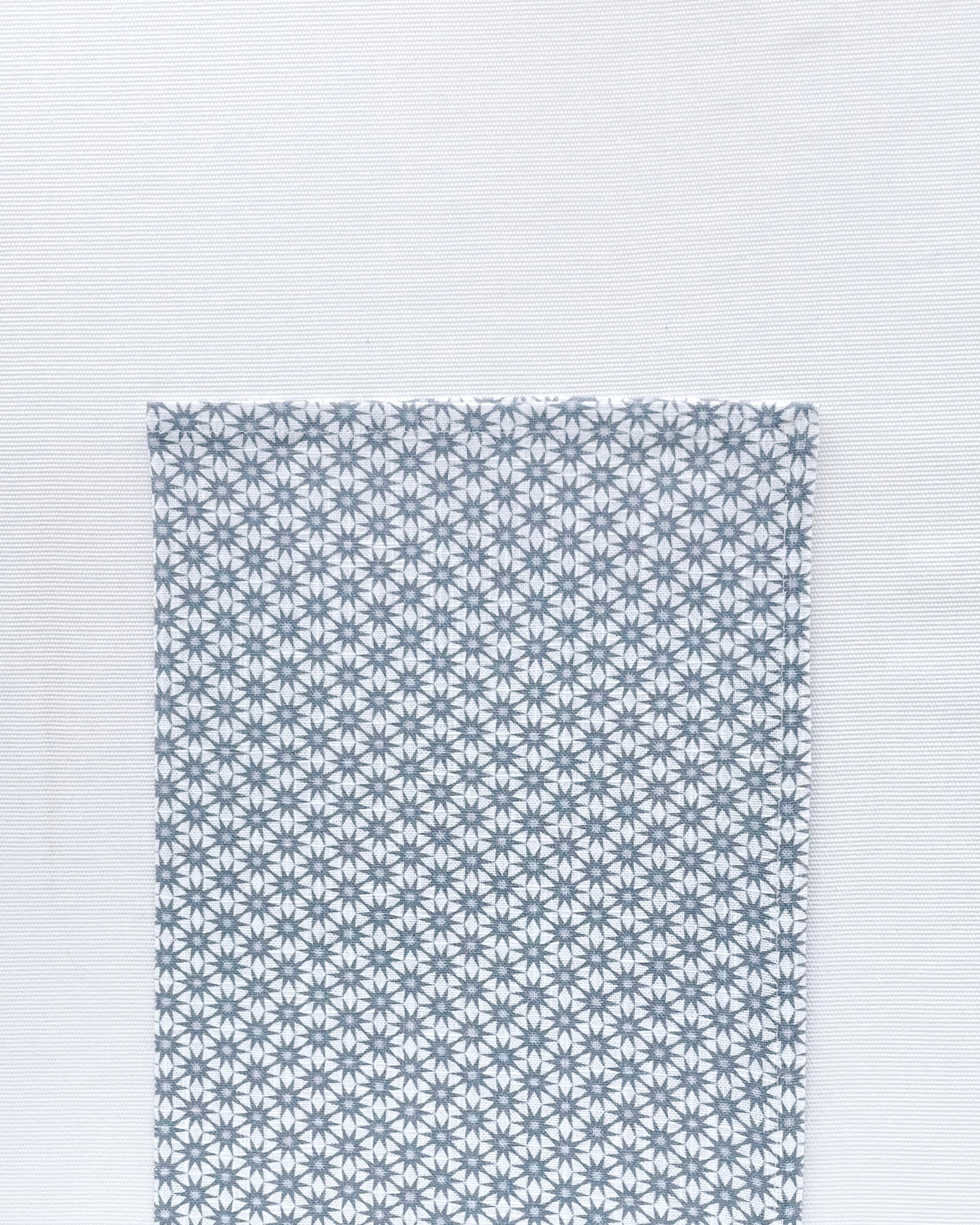 Flat lay of Starburst Denim Napkin folded in half on a white background. Napkin is white with a pattern of blue starburst laid out on top of the white hemp-linen blended material.