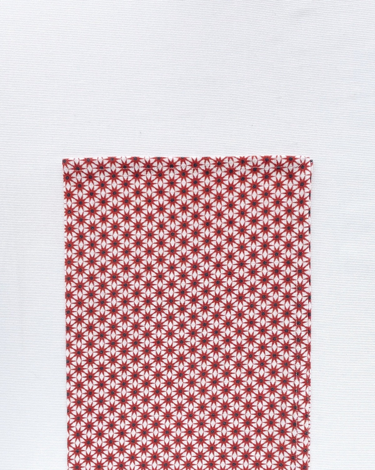 Flat lay of Starburst Rust Napkin folded in half on a white background. Napkin is white with a pattern of rust starburst laid out on top of the white hemp-linen blended material.