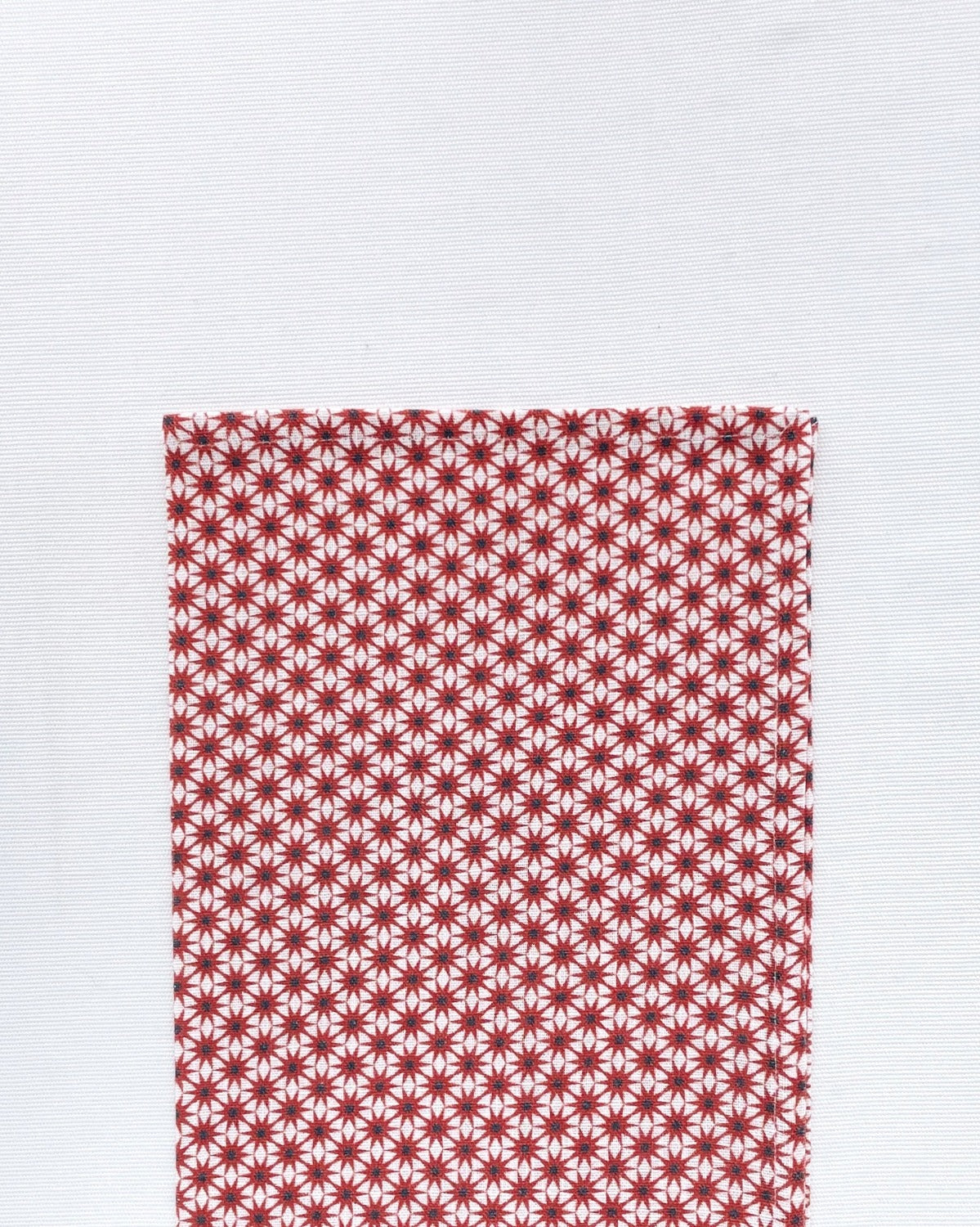Flat lay of Starburst Rust Napkin folded in half on a white background. Napkin is white with a pattern of rust starburst laid out on top of the white hemp-linen blended material.