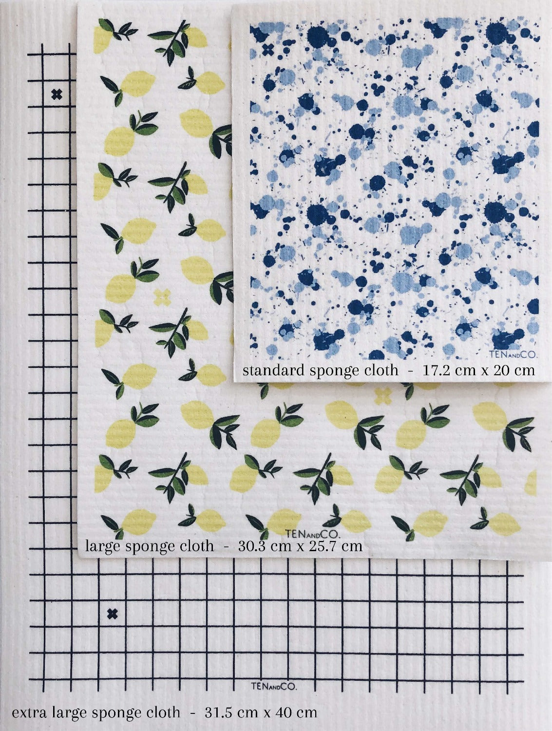 Flay lay image of sponge cloth sizes. There are 3 different sized sponge cloths laying on top of each other. On the bottom is an XL grid sponge cloth. On top of that is a large Citrus Lemon sponge cloth and then on top of that is a standard Splatter Blues sponge cloth. 